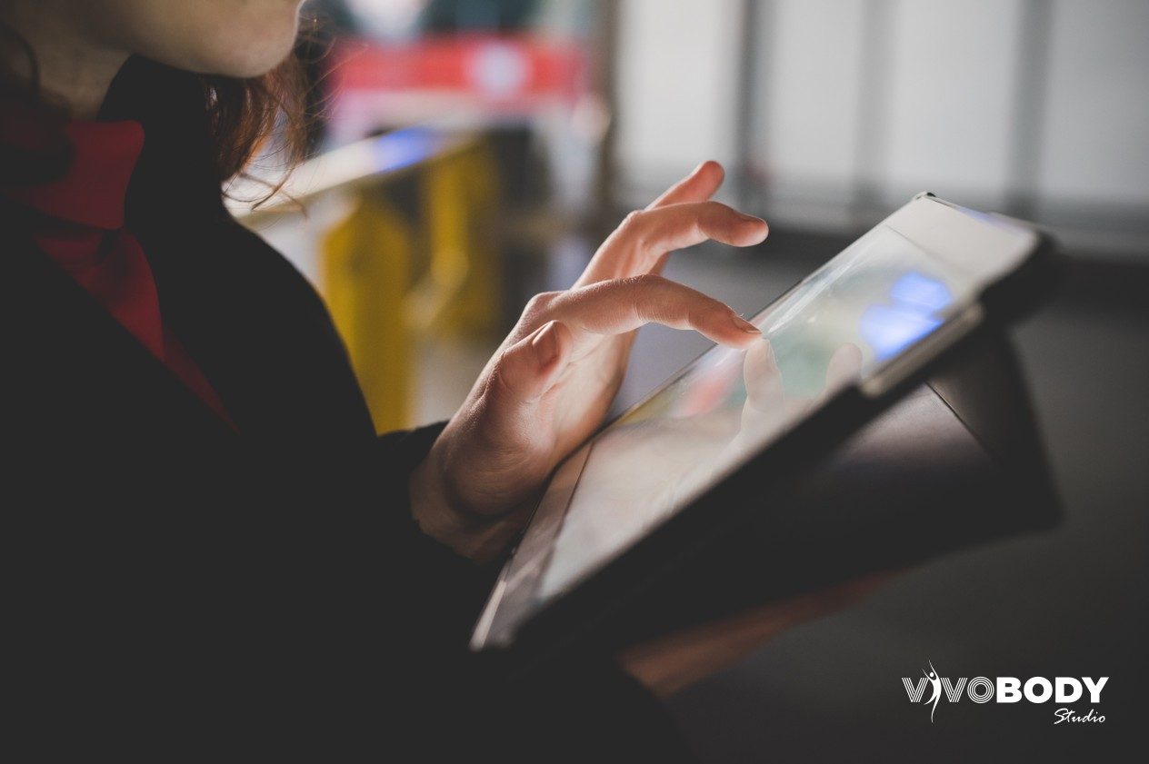 Woman using a tablet in a dark room with the screen lighting her hands