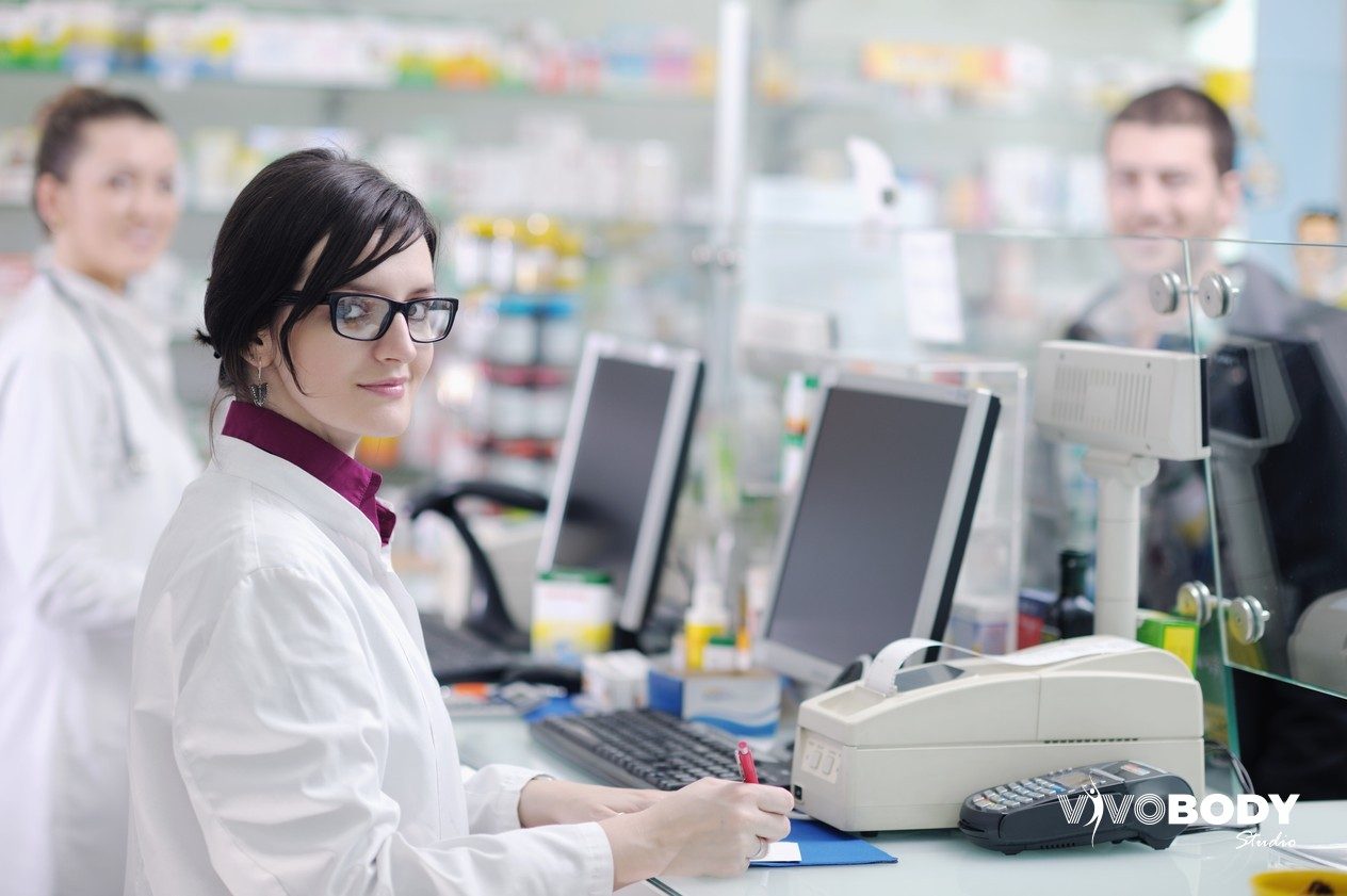 Pharmacist working at a pharmacy counter with dispensing shelves behind
